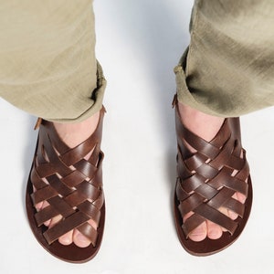 Puede incluir: Sandalias de cuero marr&oacute;n con un dise&ntilde;o tejido. Las sandalias tienen una correa que va alrededor del tobillo y una correa para los dedos.