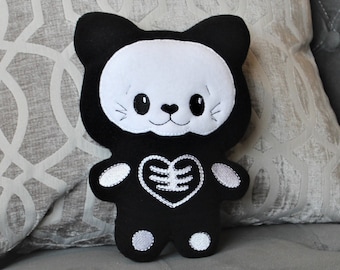 May include: A black and white plush cat toy with a skeleton design. The cat has a white face with black eyes and a black nose. The cat is wearing a black skeleton costume with a white heart-shaped bone on the chest.