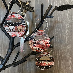 May include: Two keychains with a red, white and black design featuring a horror movie character. The keychains have a coin pocket and a silver key ring.