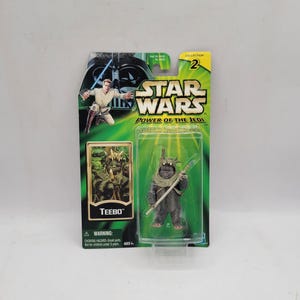 Może przedstawiać: Figurka akcji Teebo z serii Star Wars Power of the Jedi w oryginalnym opakowaniu. Karta ma zielono-czarny wzór z logo Star Wars, wizerunkiem Luke'a Skywalkera oraz przezroczystym plastikowym blistrem zawierającym figurkę Teebo.