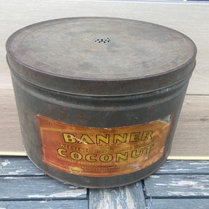 May include: A vintage metal tin container with a label that reads "Banner Sweetened Fancy Manila Coconut Specially Prepared With Delicious Coconut Milk".