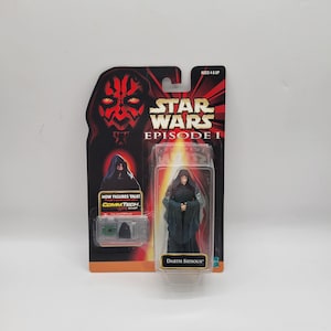 May include: A Star Wars Episode I Darth Sidious action figure in its original packaging. The packaging includes the Star Wars logo, a Darth Maul illustration, and the text "NOW FIGURES TALK! COMMTECH CHIP".