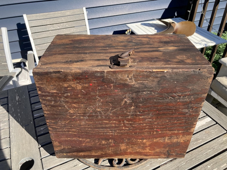 May include: A vintage wooden box with a metal latch. The box is brown and has a worn, distressed finish. The box is sitting on a wooden surface.