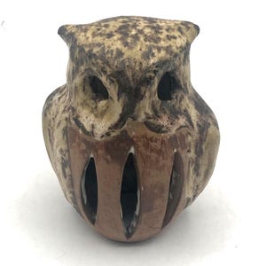Puede incluir: Figura de búho de cerámica con acabado beige y marrón moteado. El búho tiene grandes cuencas oscuras y un pecho marrón ranurado. La figura es un objeto decorativo.