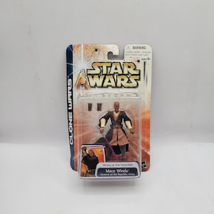 Peut inclure: Figurine Star Wars Mace Windu dans son emballage d'origine. La figurine est dans un boîtier en plastique transparent, avec le logo Star Wars et le texte "Clone Wars" sur la carte. La figurine porte une tenue sombre et tient un sabre laser violet.