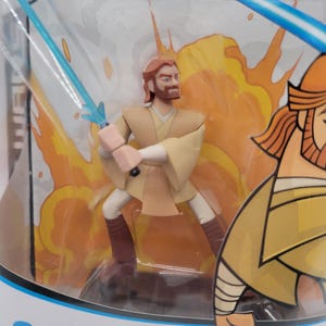 May include: A Star Wars Obi-Wan Kenobi action figure in a clear plastic package. The figure is in a dynamic pose with two blue lightsabers. The background features orange and yellow flames. The packaging has the character's name printed on it.