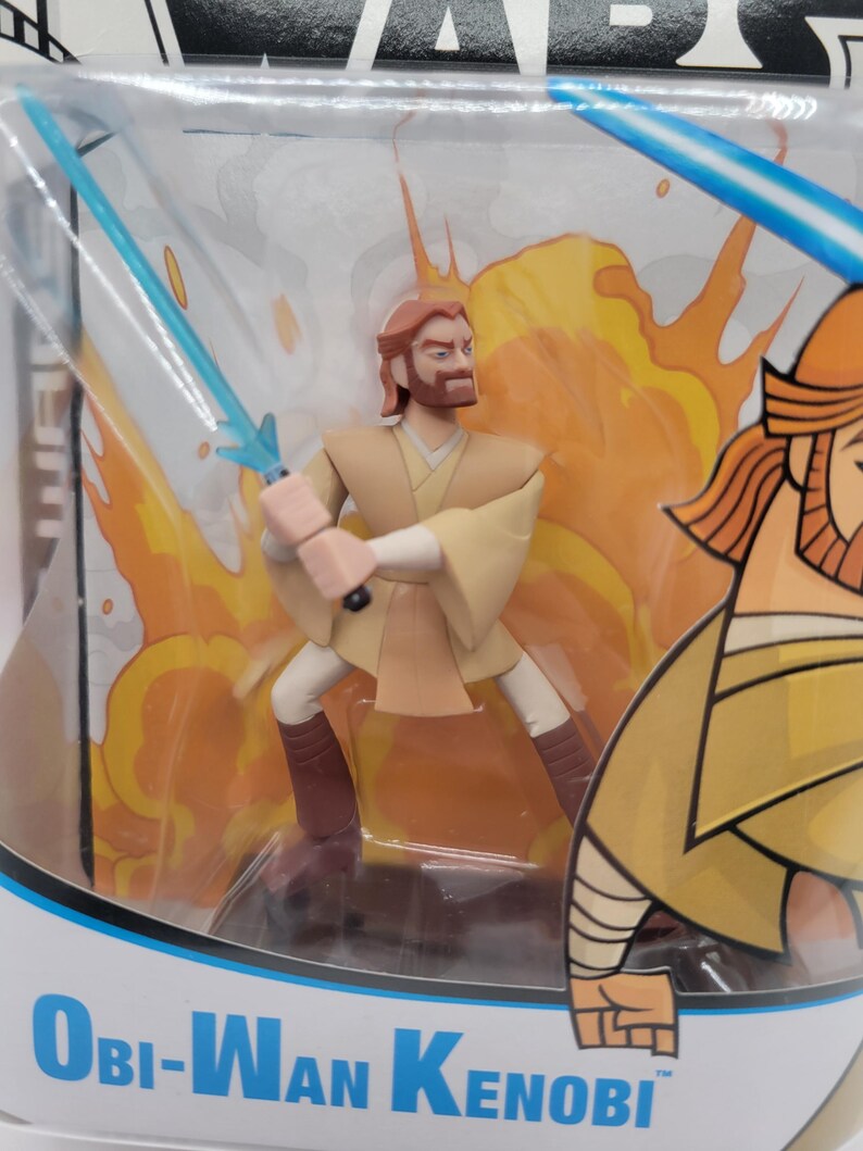 May include: A Star Wars Obi-Wan Kenobi action figure in a clear plastic package. The figure is in a dynamic pose with two blue lightsabers. The background features orange and yellow flames. The packaging has the character's name printed on it.