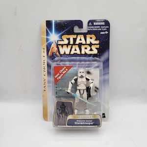Op de afbeelding: Een Star Wars Fans' Choice #4 McQuarrie Concept Stormtrooper actiefiguur in de originele verpakking. De figuur is wit en zwart, met een blauw lichtzwaard. De verpakking bevat het Star Wars logo en een waarschuwingslabel.