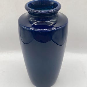 May include: A white ceramic mug with a black handle and the text "But First, Coffee" in a black, handwritten-style font. The mug is on a white surface.