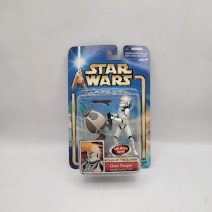May include: A Star Wars "Attack of the Clones" action figure of a Clone Trooper, packaged on a blue and white card. The figure is white with black accents and comes with a firing turret. The packaging includes the Star Wars logo and the text "Clone Trooper".