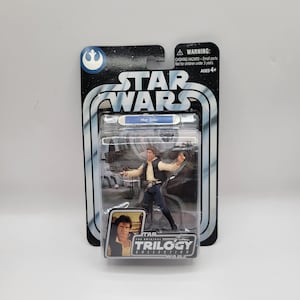 Puede incluir: Una figura de acción de Han Solo de Star Wars en su embalaje original. La figura está en una funda de plástico transparente, con el logotipo de Star Wars y "Han Solo" impresos en el embalaje. El embalaje también incluye una advertencia sobre piezas pequeñas y es para mayores de 4 años.