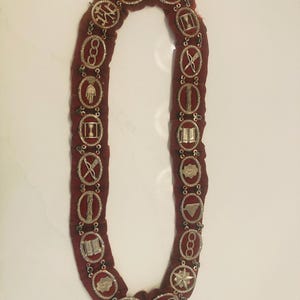 May include: A red velvet collar with silver metal embellishments. The collar features a variety of symbols, including a compass, a square, and a triangle.