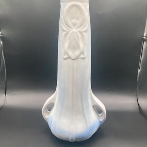 Puede incluir: Un jarrón alto, azul claro, con base acampanada y dos asas. El jarrón presenta un diseño floral en relieve en la parte delantera y detalles verticales acanalados. La parte inferior del jarrón tiene un tono azul más oscuro.