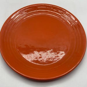 Op de afbeelding: Een ronde, oranje keramische plaat met een glanzende afwerking. De plaat heeft een licht verhoogde rand en concentrische groeven. Dit servies is geschikt voor het serveren van maaltijden.