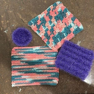 Puede incluir: Tres paños de cocina de crochet en rosa, azul y verde, y dos estropajos morados. Los paños de cocina de crochet tienen un patrón de cuadros.