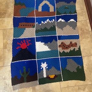 Peut inclure: Une couverture crochetée à la main avec un motif patchwork représentant diverses scènes de paysage. La couverture présente des carrés avec des images de montagnes, d'un volcan, d'un cactus et d'un feu de camp, le tout sur fond bleu. La couverture mesure environ 122 cm sur 152 cm.
