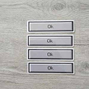May include: Four rectangular stickers arranged vertically, each featuring a light gray button design with a dark gray border and the word Ok printed in a black pixelated font centered on the surface of each individual sticker.