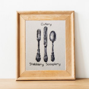 May include: A framed cross-stitch design featuring a knife, fork, and spoon with the text "Cutlery", "Stabblery", and "Scooplery".
