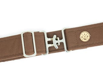 May include: A brown fabric belt featuring a silver-toned metal hook-and-loop closure mechanism and a rectangular adjustment slider. A circular gold-toned emblem is attached to the fabric, displaying the letters 'ptp' and a small animal icon.