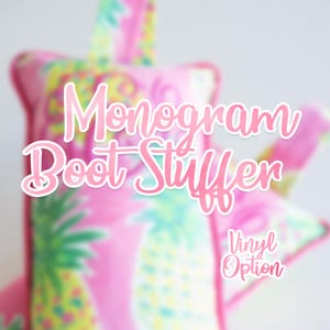Puede incluir: Un relleno para botas de color rosa con un patrón repetitivo de piñas con hojas verdes y frutas amarillas. El artículo incluye una trabilla de tela en la parte superior para colgarlo. El texto Monogram Boot Stuffer y Vinyl Option aparece en blanco.