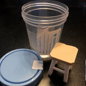 May include: A clear plastic container with a blue lid and a label that says "Biohazardous". The container is sitting on a black surface next to a small white stool.