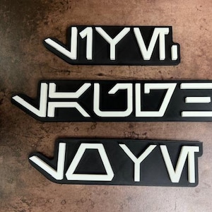 Könnte beinhalten: Drei schwarze rechteckige Schilder mit weißen Buchstaben. Die Schilder zeigen "JYVI", "JKULZE" und "JAYVI".