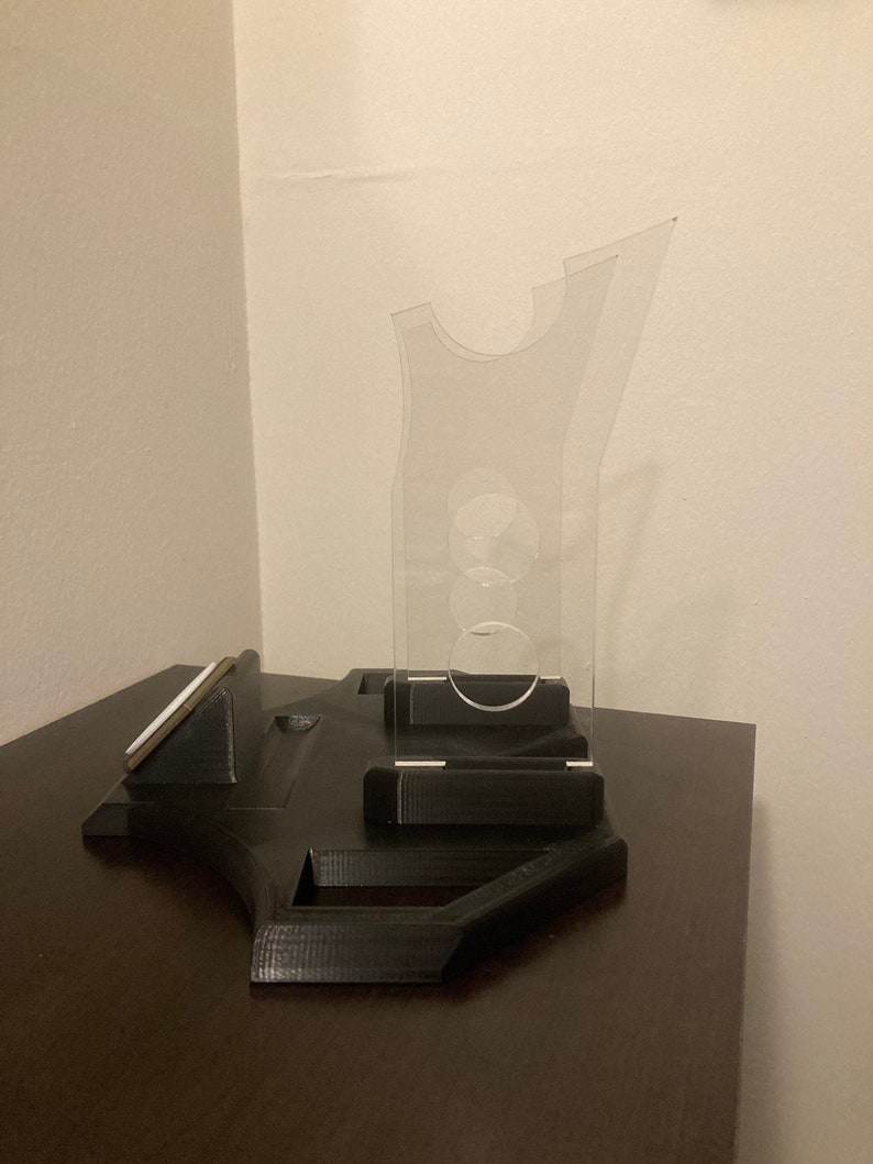 Pu&ograve; includere: Un supporto in stampa 3D nero con un supporto per telefono in plastica trasparente. Il supporto ha una fessura per un telefono e un'area rialzata per la ricarica.