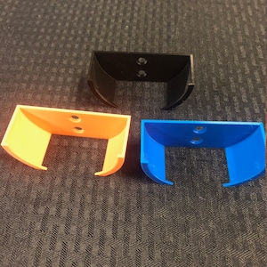 Pode incluir: Três suportes de parede, um preto, um laranja e um azul. Cada suporte tem dois furos para montagem.