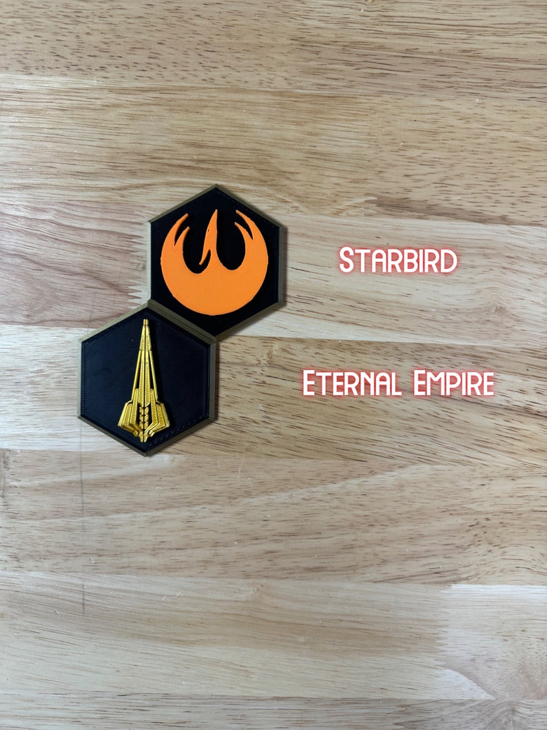 May include: Two hexagonal patches with embroidered logos. The top patch is orange and black with a stylised bird design. The bottom patch is black with a gold spaceship design. The text "STARBIRD" is above the top patch and "ETERNAL EMPIRE" is below the bottom patch.