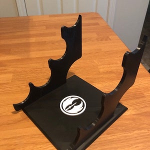 May include: Black plastic stand with a white Rebel Alliance symbol. The stand has four slots for holding items.