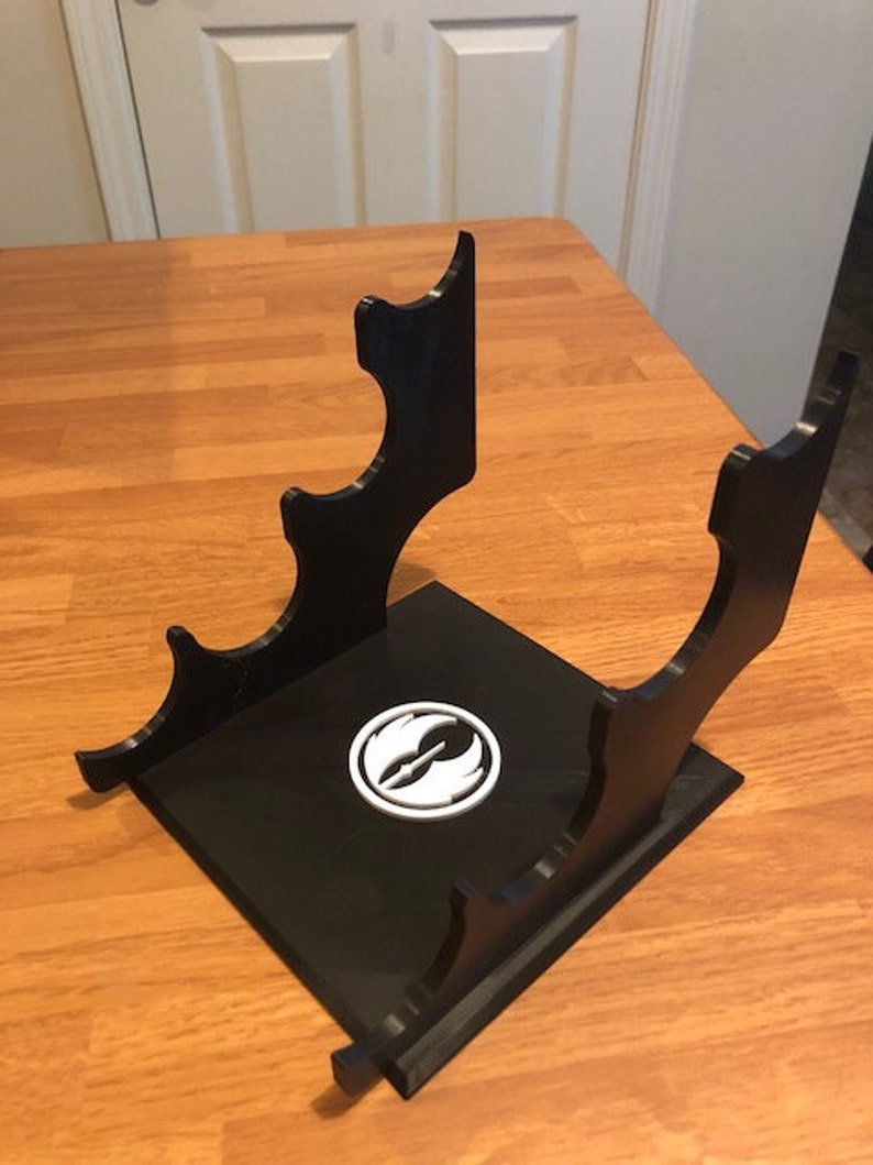 May include: Black plastic stand with a white Rebel Alliance symbol. The stand has four slots for holding items.