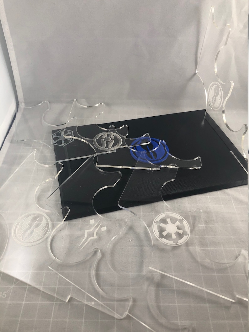 May include: A set of clear acrylic display stands featuring various Star Wars logos etched onto them. The stands are designed to hold miniature figures or other collectibles.