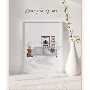 K&ouml;nnte beinhalten: Eine wei&szlig;e gerahmte Illustration eines Wohnzimmers mit einem grauen Sofa, einer Lampe, einem Beistelltisch und einer Wand mit gerahmten Kunstwerken. Die Kunstwerke umfassen einen Druck mit dem Wort "HYGGE" und einem Mond- und Sternenmotiv.