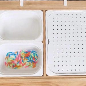 May include: A wooden tray with four white plastic containers. The top container is empty. The bottom container is filled with colorful plastic sticks. The container on the right has a perforated surface. The tray has the text "Beright" printed on the bottom.