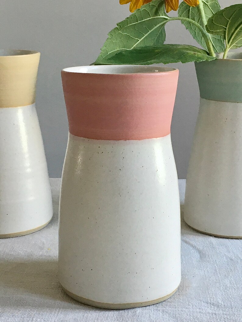 Może przedstawiać: Biały ceramiczny wazon z r&oacute;żową krawędzią. Wazon ma gładką powierzchnię i zaokrąglone dno.
