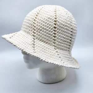 May include: A white crocheted sun hat with a wide brim. The hat is made with a simple stitch pattern and has a slightly slouchy fit.