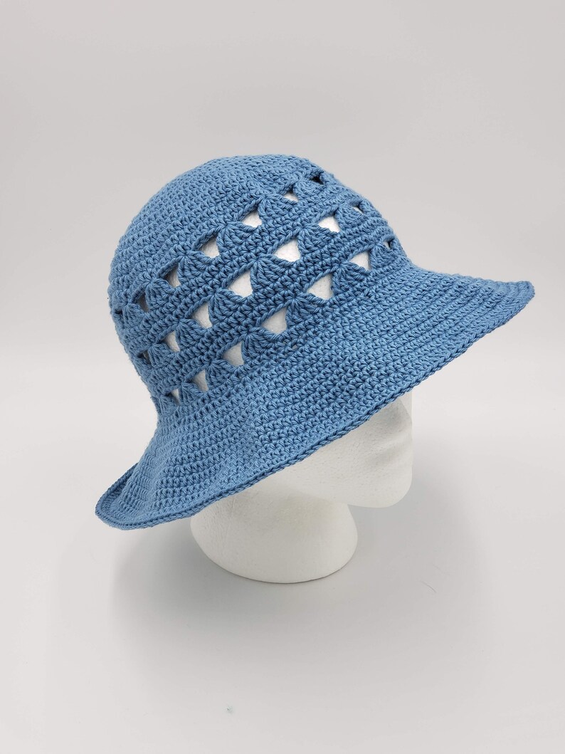 May include: A blue crocheted sun hat with a wide brim and a geometric pattern. The hat has a crocheted design with open spaces.