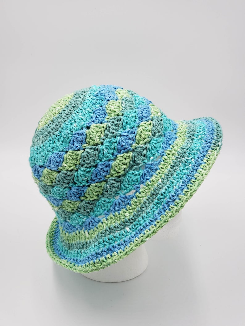 May include: A crocheted sun hat in shades of blue and green. The hat has a wide brim and is made with a textured stitch.