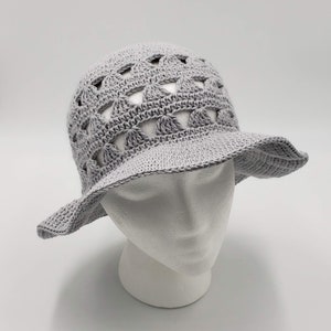 May include: A grey crochet sun hat with a wide brim and a crocheted design featuring openwork circles. The hat is on a white mannequin head.