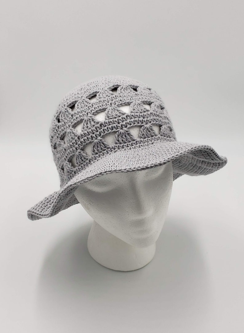 May include: A grey crochet sun hat with a wide brim and a crocheted design featuring openwork circles. The hat is on a white mannequin head.
