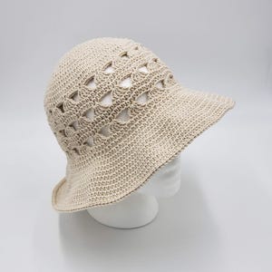May include: A beige crochet sun hat with a wide brim and a geometric pattern. The hat is made with open stitches, creating a lightweight and airy design.