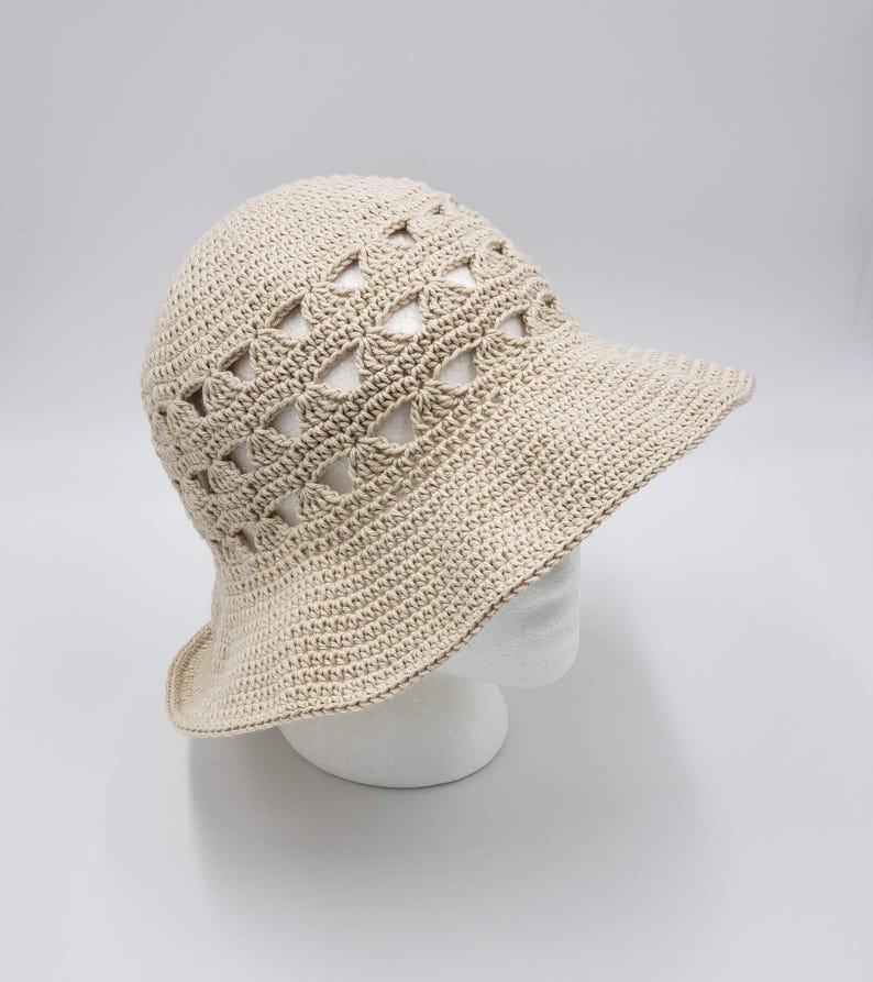 May include: A beige crochet sun hat with a wide brim and a geometric pattern. The hat is made with open stitches, creating a lightweight and airy design.