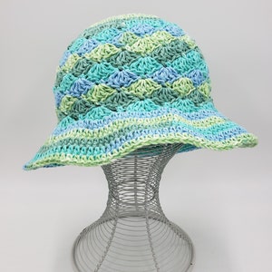 May include: A crocheted sun hat with a wide brim in shades of green and blue. The hat is displayed on a wire hat stand.