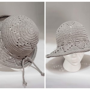May include: A light gray crochet sun hat featuring a wide brim, a rounded crown, and a decorative woven band detail. The hat is constructed with a repeating openwork stitch pattern throughout the crown and brim, finished with two thin ties.