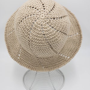 May include: A beige crocheted sun hat with a wide brim and a circular pattern of holes on the crown.