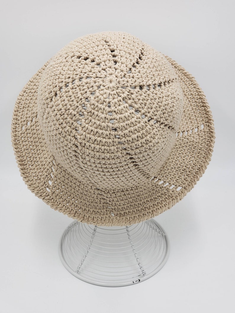 May include: A beige crocheted sun hat with a wide brim and a circular pattern of holes on the crown.