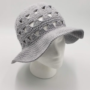 May include: A grey crochet sun hat with a wide brim and a geometric pattern. The hat has openwork details, creating a lightweight and airy design.
