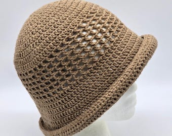 Puede incluir: Un sombrero de cubo de ganchillo de color canela con un ala pequeña. El sombrero está hecho de un material tejido de tejido abierto. El sombrero se muestra sobre una cabeza de maniquí blanca sobre un fondo blanco.
