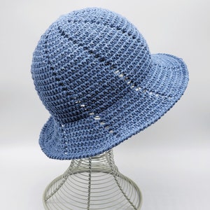 May include: A light blue crocheted sun hat with a wide brim. The hat is on a wire hat stand.