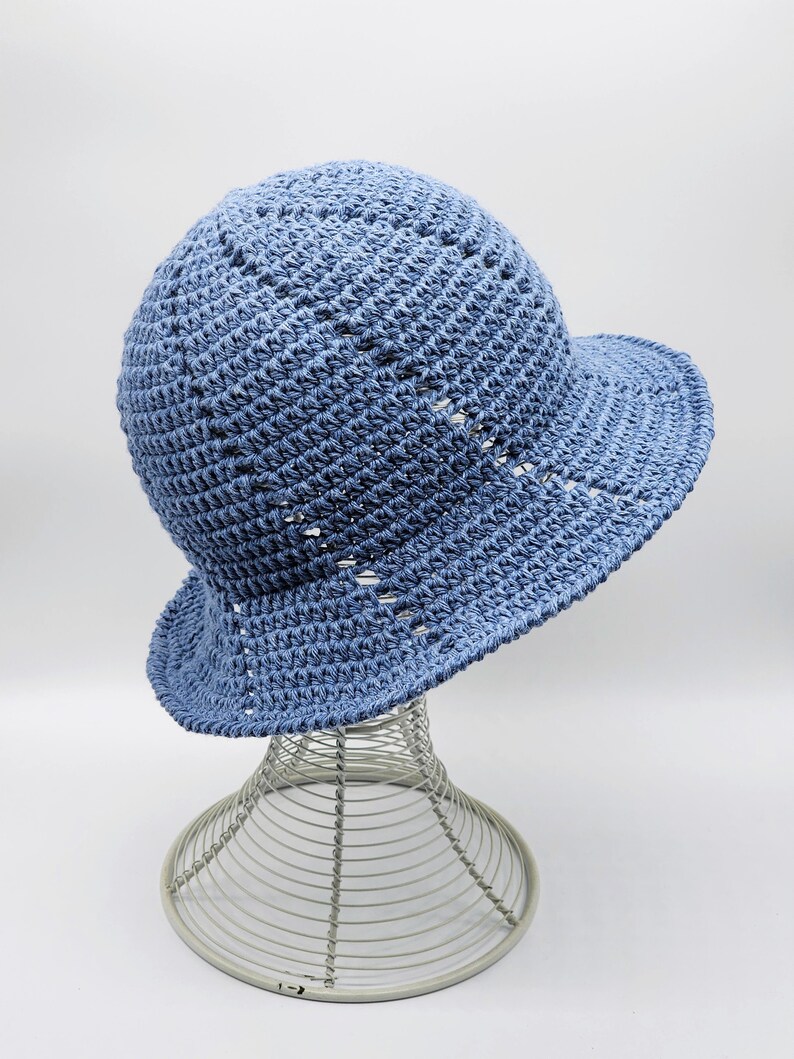 May include: A light blue crocheted sun hat with a wide brim. The hat is on a wire hat stand.